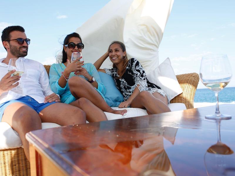 Tři uvolnění lidé na lodi s nápoji, moře v pozadí.