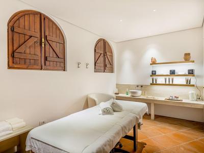 Lichte massageruimte met houten vloer, witte muren en rustieke houten ramen.