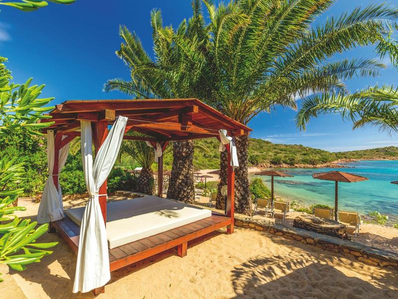 Gezellig strandbed onder palmbomen met uitzicht op de blauwe zee op een zonnige dag.