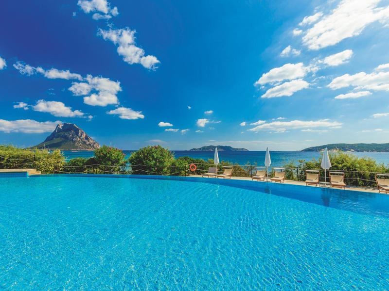 Groot zwembad met uitzicht op bergen en meer onder een blauwe lucht met wolken.