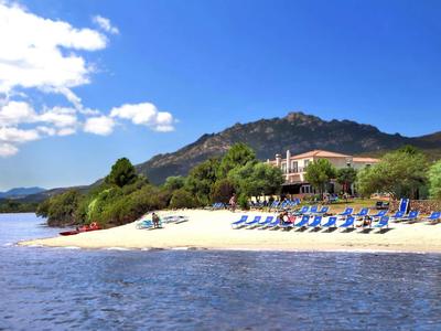 Strand mit blauem Himmel, Liegestühlen und einem Hotel am Fuße eines bewaldeten Hügels.