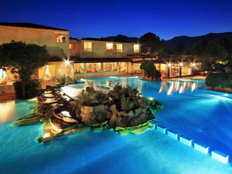Piscine d'hôtel illuminée la nuit avec architecture méditerranéenne et montagnes environnantes