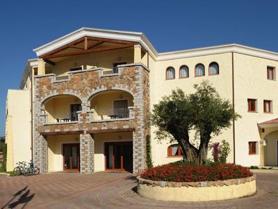 Großes gelbes Haus mit Steinverkleidung, Balkon und rundem Blumenbeet mit Baum davor.