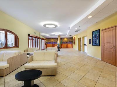 Heller, weitläufiger Raum mit gelben Wänden, beigem Sofaset, großen Fenstern und Fliesenboden.