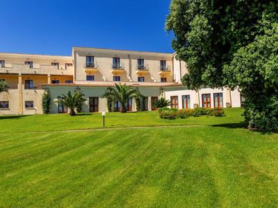 Großes gelbes Gebäude mit mehreren Fenstern, grüner Rasen und Bäume bei blauem Himmel.