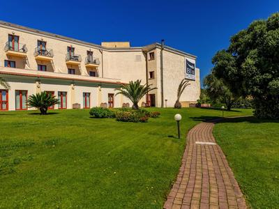 Edificio dell'hotel con facciata gialla, piccoli balconi e giardino curato sotto un cielo blu.