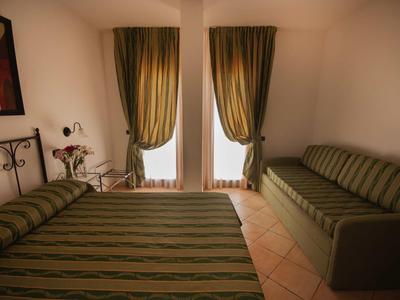 Zimmer mit grün gestreiftem Bett, Sofa, Vorhängen und zwei Fenstern, helle Wände und Bodenfliesen.