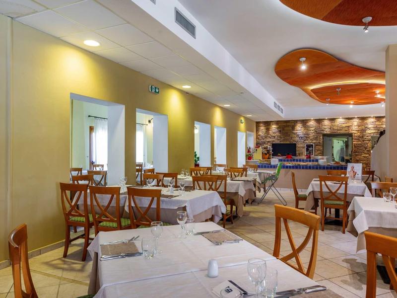 Hell eingerichtetes Restaurant mit weißen Tischtüchern, Holzmöbeln und moderner Deckenlampe.