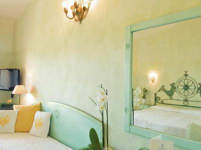 Pohodlný hotelový pokoj s pastelově zeleným nábytkem, postelí a ozdobným zrcadlem odrážejícím místnost.