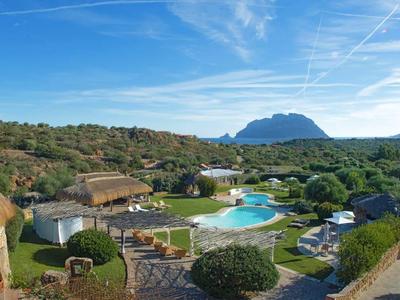 Rezort s kulatými chatkami, bazénem, zelení a horou v pozadí pod modrou oblohou.