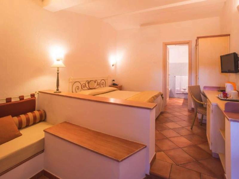 Příjemný hotelový pokoj s posezením, dvěma postelemi a stolkem s TV, teplé osvětlení.