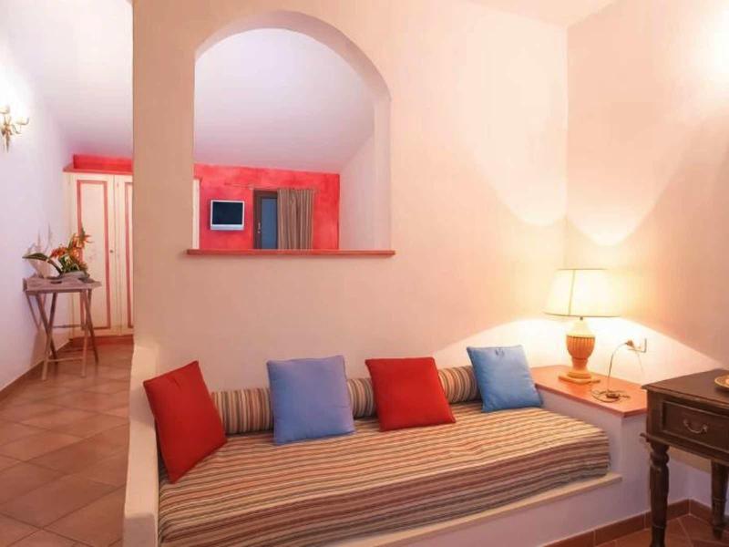 Pohodlný hotelový pokoj s pruhovanou postelí, barevnými polštáři, teplým osvětlením a jednoduchým zařízením.