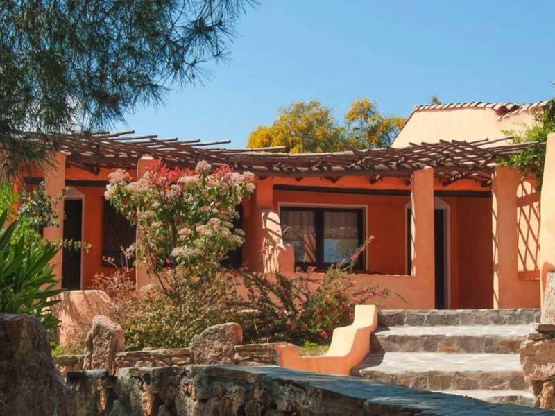 Vítající terasa se schody, rostlinami a oranžovou fasádou pod jasnou oblohou.