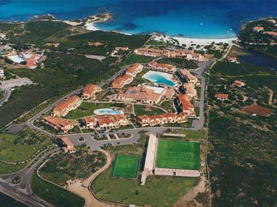 Letecký pohled na hotel s bazény, plážemi a sportovními hřišti obklopený zelení.