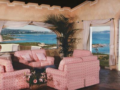 Pohodlný salonek s růžovými křesly s výhledem na moře a ostrovy skrz velká okna.