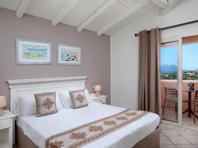 Světelná ložnice s bílou postelí, dekorativními polštáři, nočními stolky a přístupem na balkon.