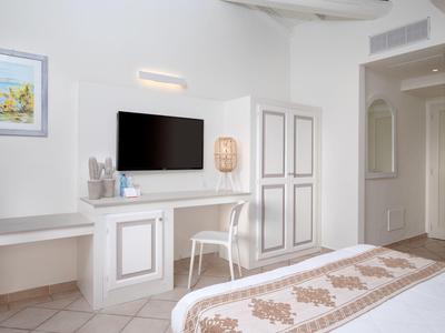 Světly hotelový pokoj s psacím stolem, televizí a dekorativní postelí