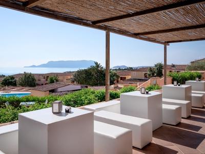 Terrasse couverte avec tables et bancs blancs, vue sur jardins, maisons et montagnes en arrière-plan.