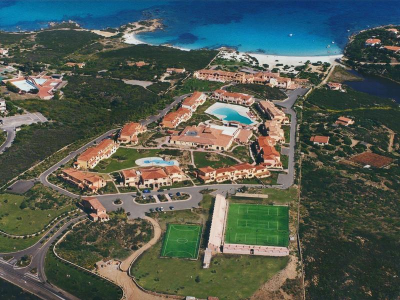 Letecký pohled na hotel s bazény, plážemi a sportovními hřišti obklopený zelení.