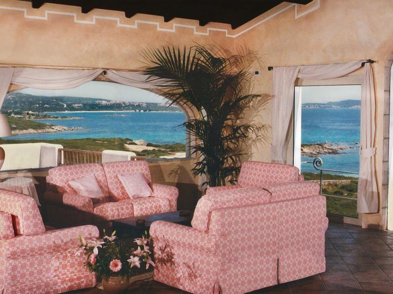 Pohodlný salonek s růžovými křesly s výhledem na moře a ostrovy skrz velká okna.