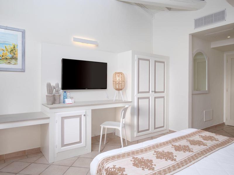 Světly hotelový pokoj s psacím stolem, televizí a dekorativní postelí