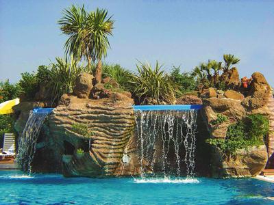 Cascata artificiale che si getta in una piscina blu chiaro con rocce e piante tropicali.