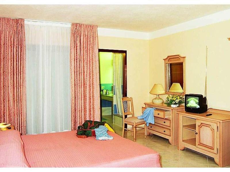 Camera d'hotel luminosa con letto matrimoniale, tende, mobili in legno e TV.