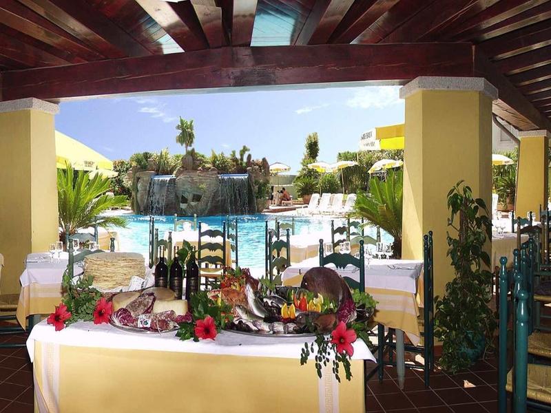 Terrazza coperta con tavoli apparecchiati che si affacciano su una piscina dell'hotel al sole.