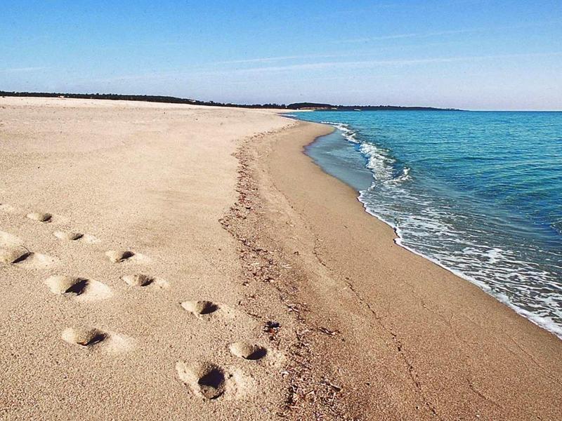 Spiaggia sabbiosa con impronte di piedi accanto al mare blu calmo sotto un cielo sereno