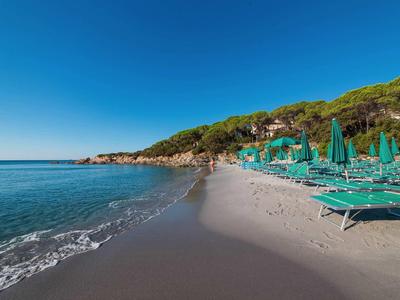 Prázdná pláž s lehátky a slunečníky vedle čisté modré vody pod jasnou oblohou.