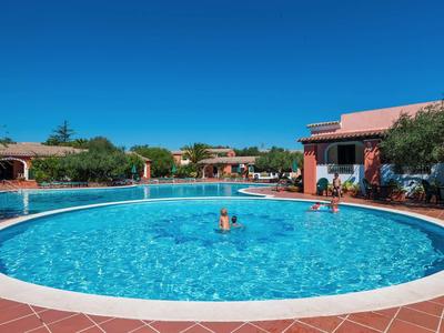 Kruhový bazén v hotelovém komplexu pod jasnou modrou oblohou.