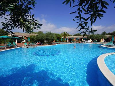 Großer blauer Pool mit Sonnenschirmen und Bäumen unter blauem Himmel.