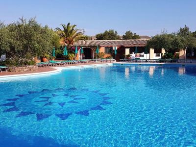 Velký hotelový bazén se slunečními lehátky a palmami v tropickém prostředí.