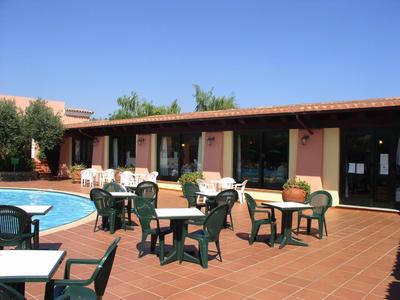 Hotelové nádvoří s bazénem, několika stoly a židlemi na červené cihlové podlaze pod jasnou oblohou.