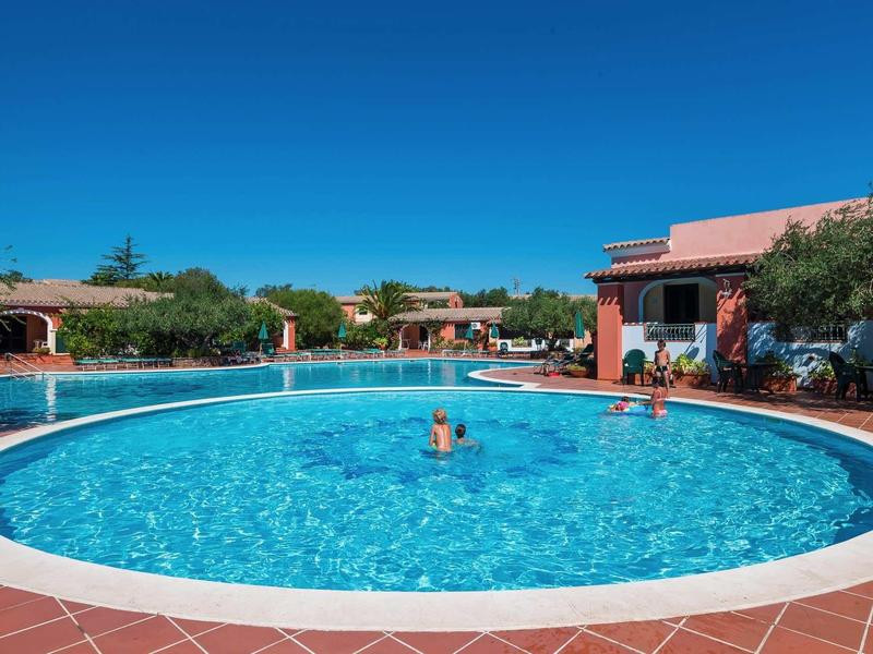 Kruhový bazén v hotelovém komplexu pod jasnou modrou oblohou.