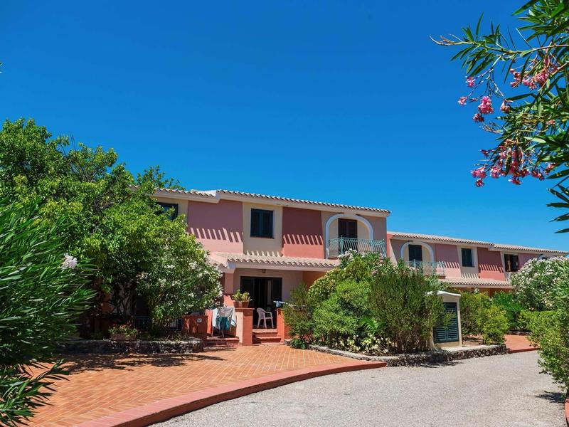 Růžová budova s terasou a bujnou zelení pod jasně modrou oblohou.