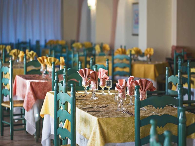 Restaurace se zelenými židlemi a stoly zdobenými žlutými a červenými ubrusy a ubrousky.