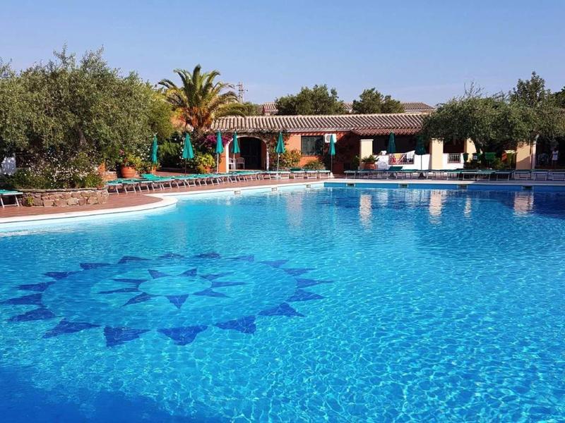 Velký hotelový bazén se slunečními lehátky a palmami v tropickém prostředí.