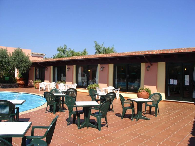 Hotelové nádvoří s bazénem, několika stoly a židlemi na červené cihlové podlaze pod jasnou oblohou.