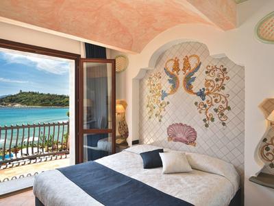 Slaapkamer met artistiek hoofdeinde en open balkon met uitzicht op zee.