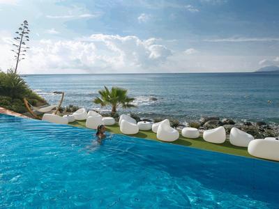 Infinityzwembad met uitzicht op zee en ligstoelen langs de kust.