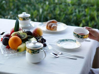 Ontbijttafel met fruit, gebak en thee buiten met groene achtergrond