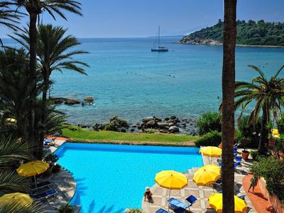Strandhotel met zwembad, palmbomen en uitzicht op de blauwe zee met zeilboot.