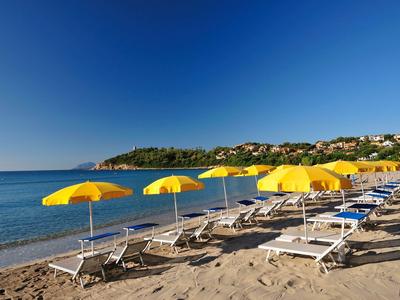 Zandstrand met meerdere gele parasols en witte ligstoelen bij kalme zee.