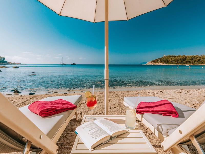 Strandstoelen met handdoeken en drankjes onder een parasol aan zee.