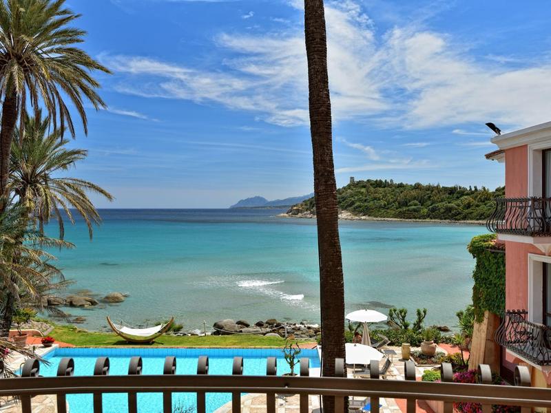 Uitzicht op een zwembad met palmbomen en zee op de achtergrond onder een blauwe lucht.