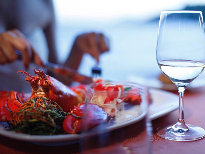 Wijnglas naast een bord met verse kreeften in een restaurant aan het water.