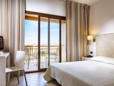 Hotelzimmer mit Doppelbett, Stuhl, Fernseher und Balkon mit Blick ins Freie.