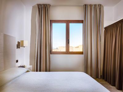 Helles Hotelzimmer mit großem Fenster, weißen Wänden und braunen Vorhängen neben einem Bett.