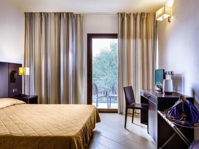 Hell beleuchtetes Hotelzimmer mit großem Bett, Schreibtisch und Blick auf den Garten.